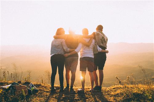 Four students seen from the back look toward sunset from hillside 