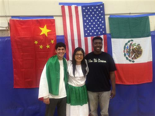 Three English Language students stand in front of flags at special event 
