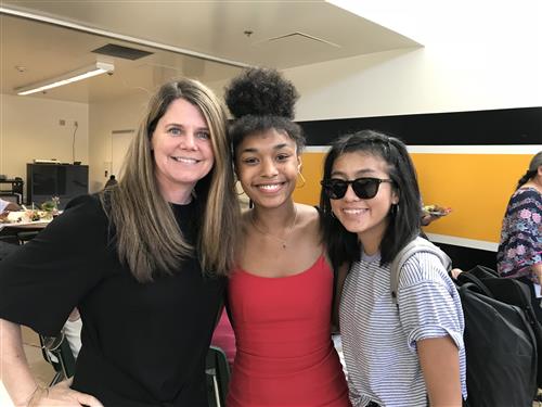 Happy female teacher poses with two female graduating seniors 